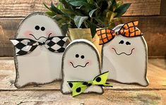 three white ghost decorations with black and yellow bows on them sitting next to a potted plant