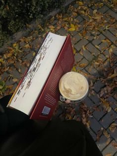 a person is holding a book and a coffee cup in their hand on the sidewalk