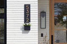 a house number sign mounted to the side of a white building with flowers in it