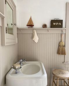 a white sink sitting under a bathroom mirror next to a wooden stool and wall hanging