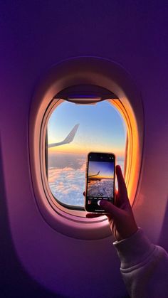 a person holding up a cell phone while looking at the sky through an airplane window