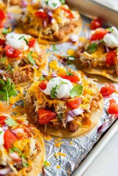 some tacos are sitting on top of tin foil and garnished with toppings