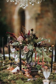 an arrangement of flowers and candles on a mossy table cloth with greenery in the center