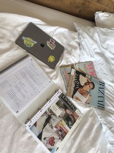 an open notebook and several magazines on a bed