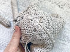 a crocheted bag is being held up by someone's hand on a white wooden surface