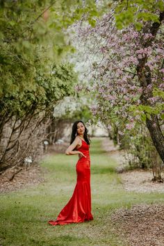 a woman in a long red dress standing under a tree with pink flowers on it