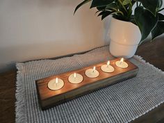 four tealight candles sit on a wooden tray next to a potted plant