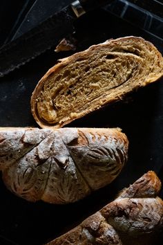 two loaves of bread sitting on top of a black counter next to a knife