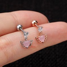 a pair of pink heart shaped earrings on someone's finger with diamond accenting