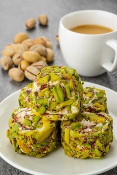 some food on a white plate next to a cup of coffee and nuts in the background