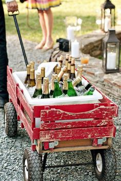 a red wagon filled with lots of bottles of beer on top of a gravel ground