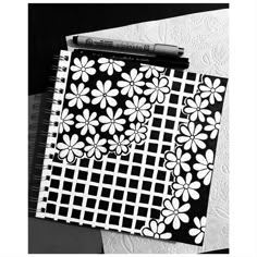 a black and white photo of a notebook with flower designs on it, next to a crayon marker