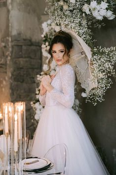 a woman in a wedding dress holding an umbrella over her head while standing next to a table with candles and flowers