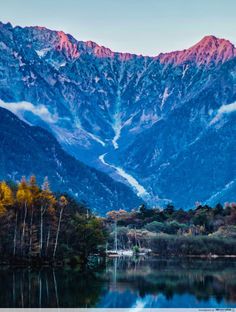 the mountains are covered in snow and clouds as seen from a lake on a clear day