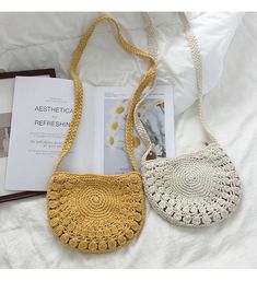 two crocheted purses sitting on top of a bed next to an open book