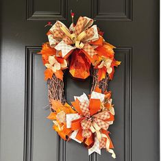 an orange and white wreath on a black door with pumpkins hanging from the front