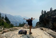 a woman standing on top of a rocky mountain with her arms outstretched in the air