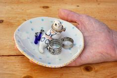 a person's hand holding a small plate with two rings and a dog figurine on it