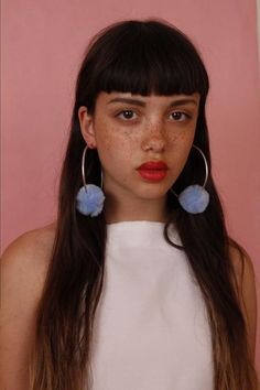 a woman with freckles on her face wearing blue earrings and a white top