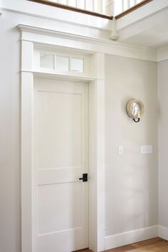 an empty room with white walls and wooden flooring is pictured in this image, there is a clock on the wall next to the door