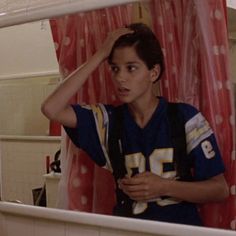 a young boy in a football uniform looking at himself in the mirror with his hand on his head