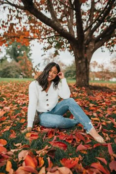 a woman sitting on the ground in front of a tree with leaves all around her