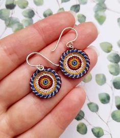 a pair of handmade earrings in blue, orange and white with an evil eye design