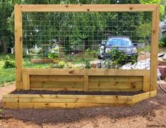 a wooden garden bed with plants growing in it and a car parked behind the fence