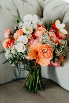 an orange and white bouquet sitting on top of a gray couch next to a pillow