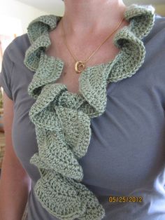 a woman is wearing a green crocheted scarf with a gold necklace on her neck