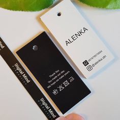 a hand holding a black and white tag next to a green leaf with the word alenka on it