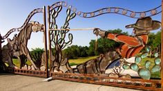 a large metal gate with horses and cactuses painted on it's sides, in front of a grassy field