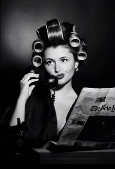 a woman with curls on her hair is talking on the phone and holding a newspaper