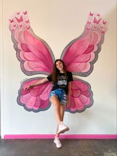 a woman posing in front of a wall with a pink butterfly on it's wings