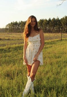 a woman standing in the middle of a field wearing white cowboy boots and a dress