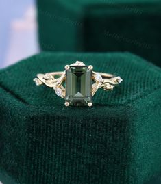 an emerald colored stone ring sitting on top of a green velvet box with gold trimmings