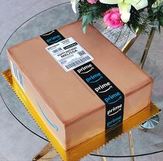 an amazon box cake sitting on top of a glass table with flowers in the background