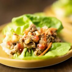 lettuce wraps with meat and vegetables on a yellow plate sitting on a wooden table