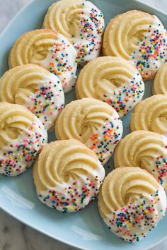 butter cookies with white frosting and sprinkles are on a blue plate