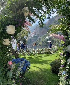 people are standing under an arch in the grass with flowers on it and one person is holding an umbrella