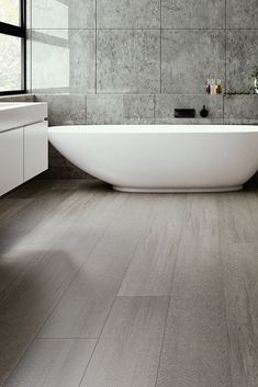 a large white bath tub sitting next to a window in a bathroom with wooden floors