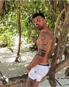 a man with tattoos sitting on a tree branch