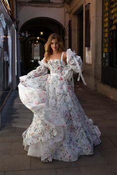 a woman is walking down the street in a white dress with floral print on it