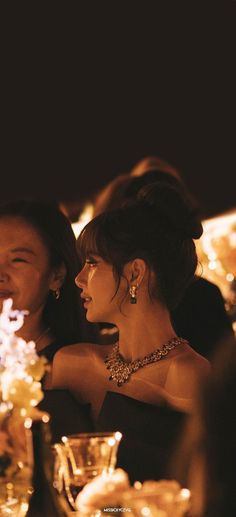 two women sitting at a table with wine glasses and flowers in front of them,