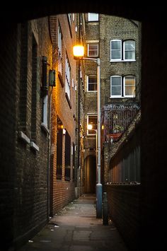 an alley way with brick buildings and street lights on either side, at night time