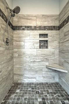 a walk in shower sitting next to a tiled floor and wall with gray tiles on the walls