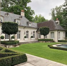 a large house with hedges around it and a pool in the front yard that is surrounded by trees