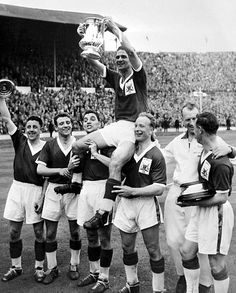 a group of men standing on top of a soccer field holding up a trophy in front of them