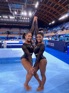 two women in black leotards standing next to each other on a blue floor