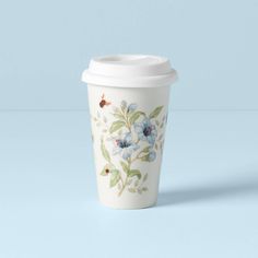 a white coffee cup with blue flowers painted on the side and green leaves around it